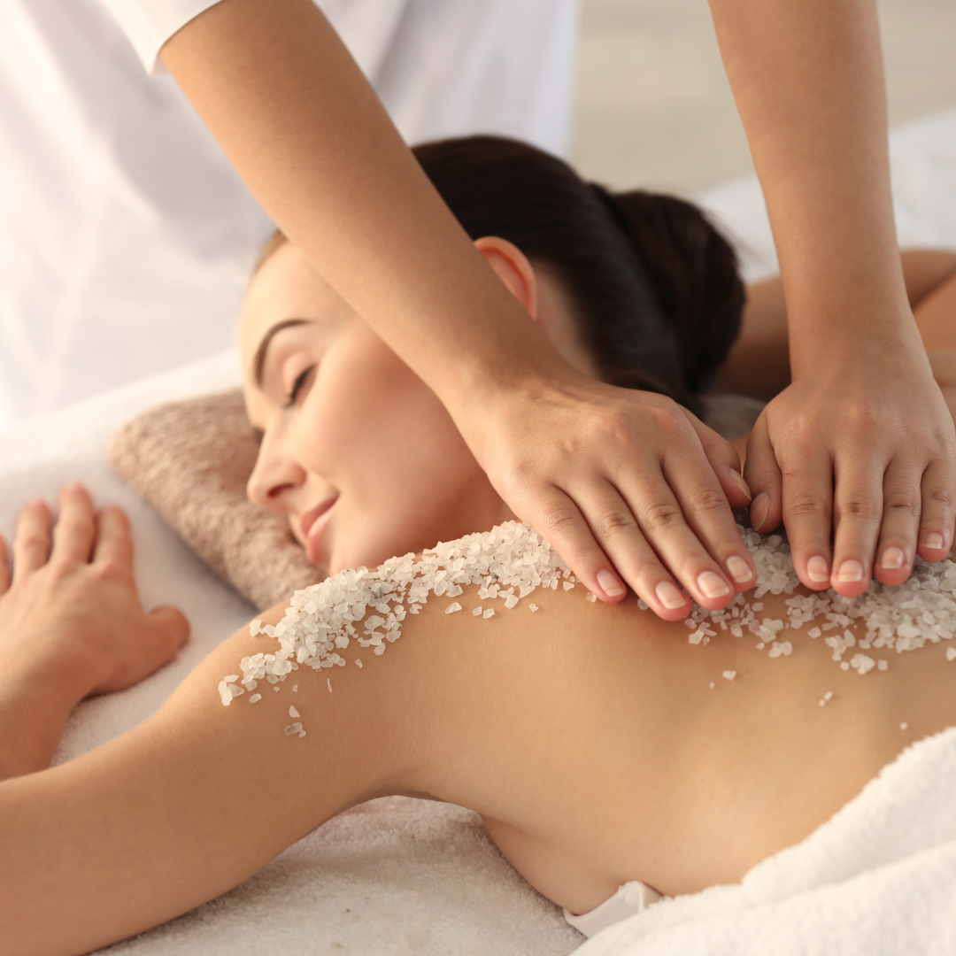 Esthetician spreading full body scrub on a woman's back.