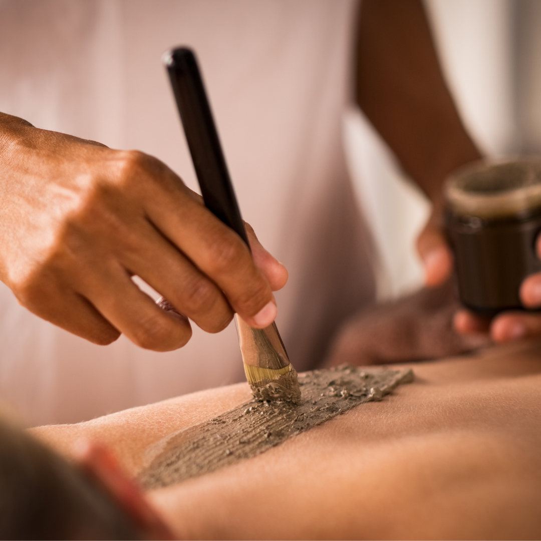 Esthetician applying algae scrub to a woman's back.